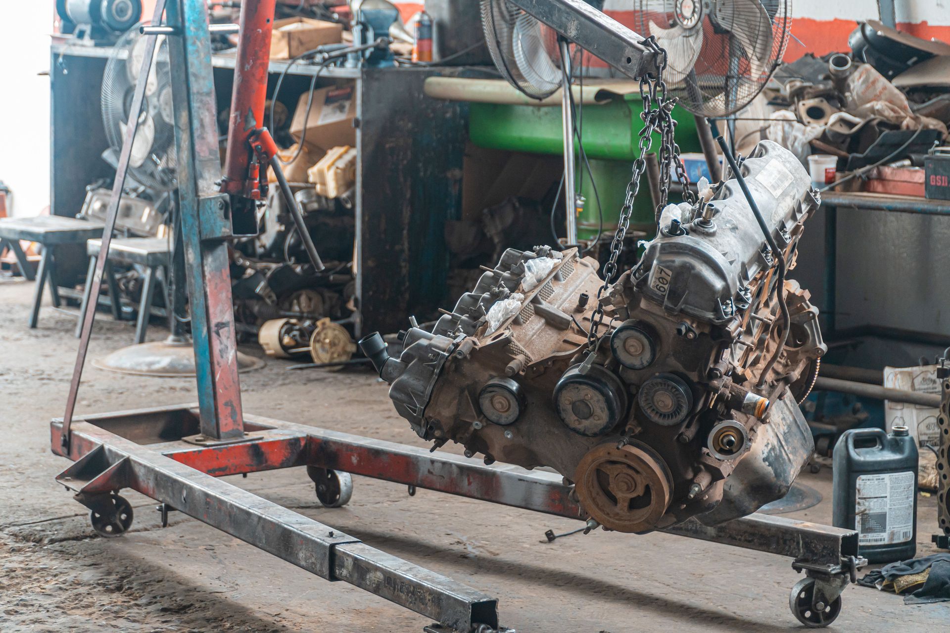 Close-up of a car engine hoisted in a mechanic's workshop, showcasing industrial tools.